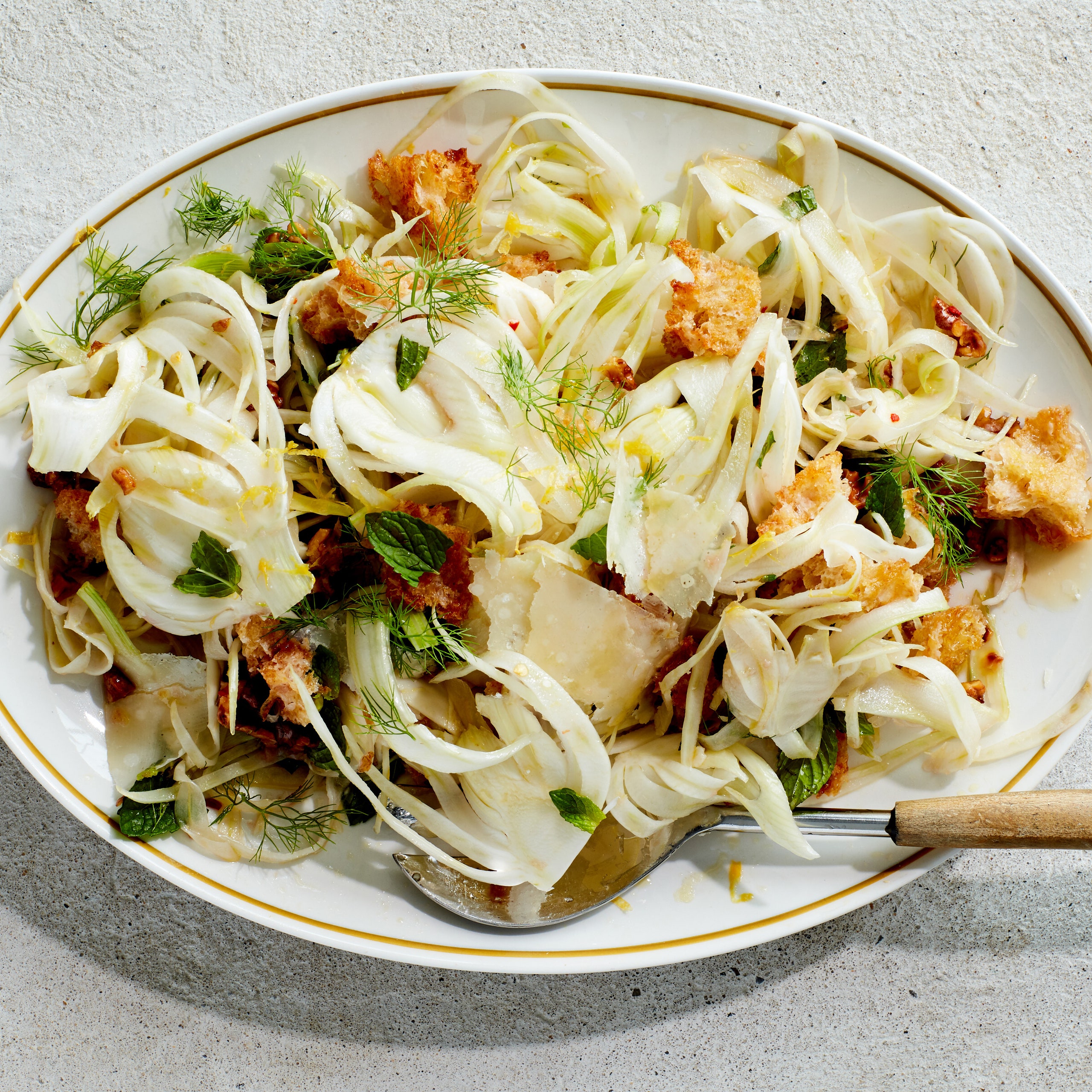 An oval platter filled with shaved fennel walnuts croutons and torn fresh mint.